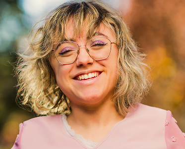 closeup-support-hands 1 (1) A smiling woman wearing glasses, a pink shirt, and makeup, radiating confidence and joy. She appears to have a disability.
