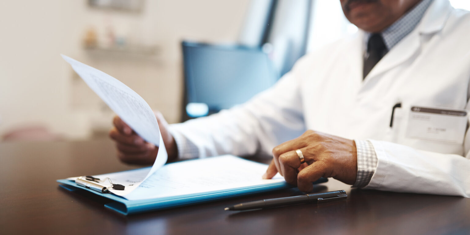 Mature, man or doctor with documents for medical records, policy or insurance on desk at hospital. Male person, employee or healthcare worker with paperwork or clipboard for life cover or application.