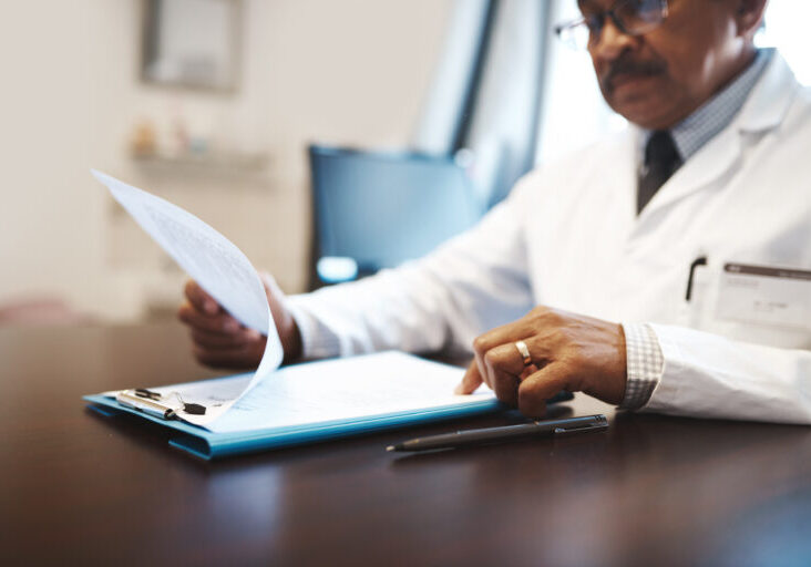 Mature, man or doctor with documents for medical records, policy or insurance on desk at hospital. Male person, employee or healthcare worker with paperwork or clipboard for life cover or application.