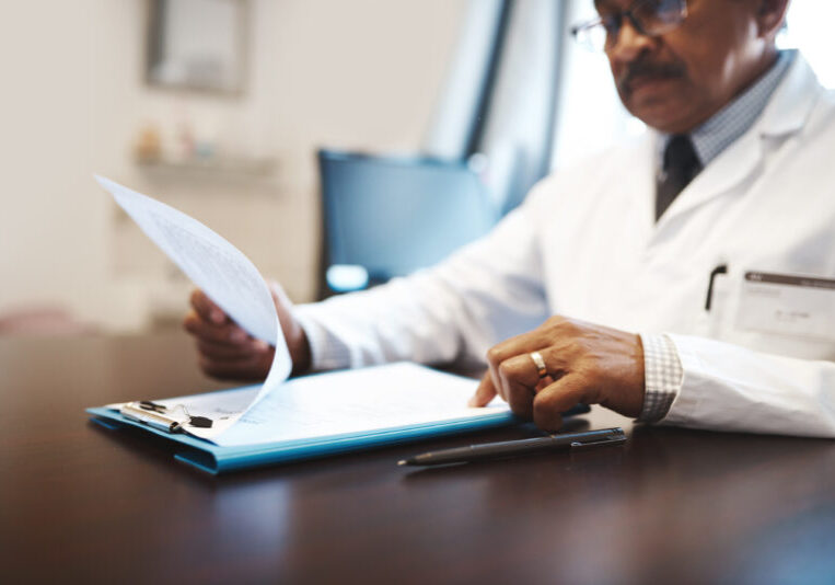 Mature, man or doctor with documents for medical records, policy or insurance on desk at hospital. Male person, employee or healthcare worker with paperwork or clipboard for life cover or application.