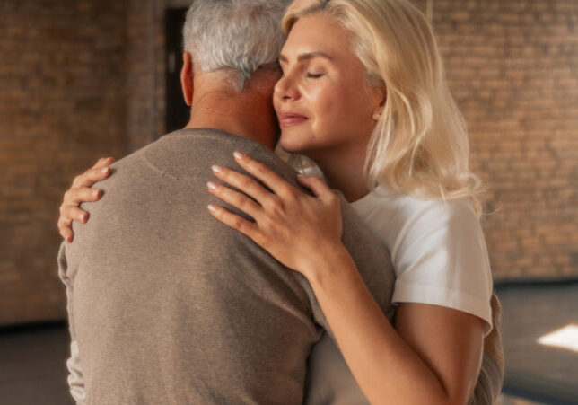 An older man and woman hugging, with only the back of the man visible.