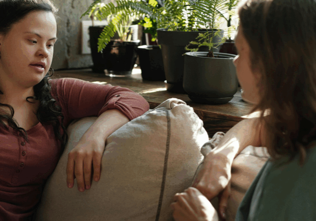 Two women sitting on a couch having a conversation, one woman with Down syndrome, appearing to be in a counseling session.