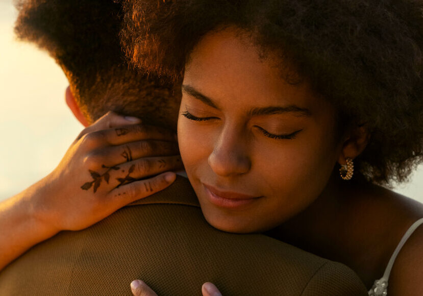A woman smiling as she hugs a man, with only the back of the man visible.