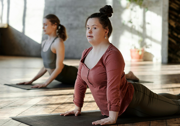 A woman with Down syndrome and another woman stretching together on an exercise mat.