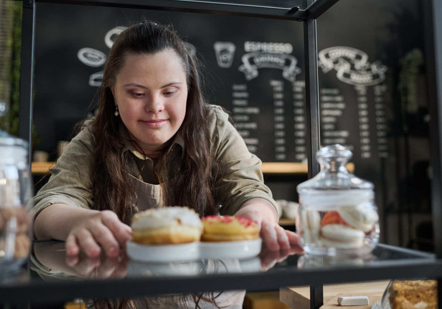 Waitress putting tasty donuts on tray A young girl with Down syndrome working at a café.